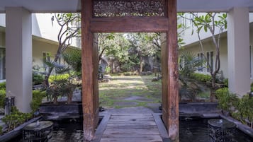 A wooden archway leading to a garden with a water feature and potted plants.