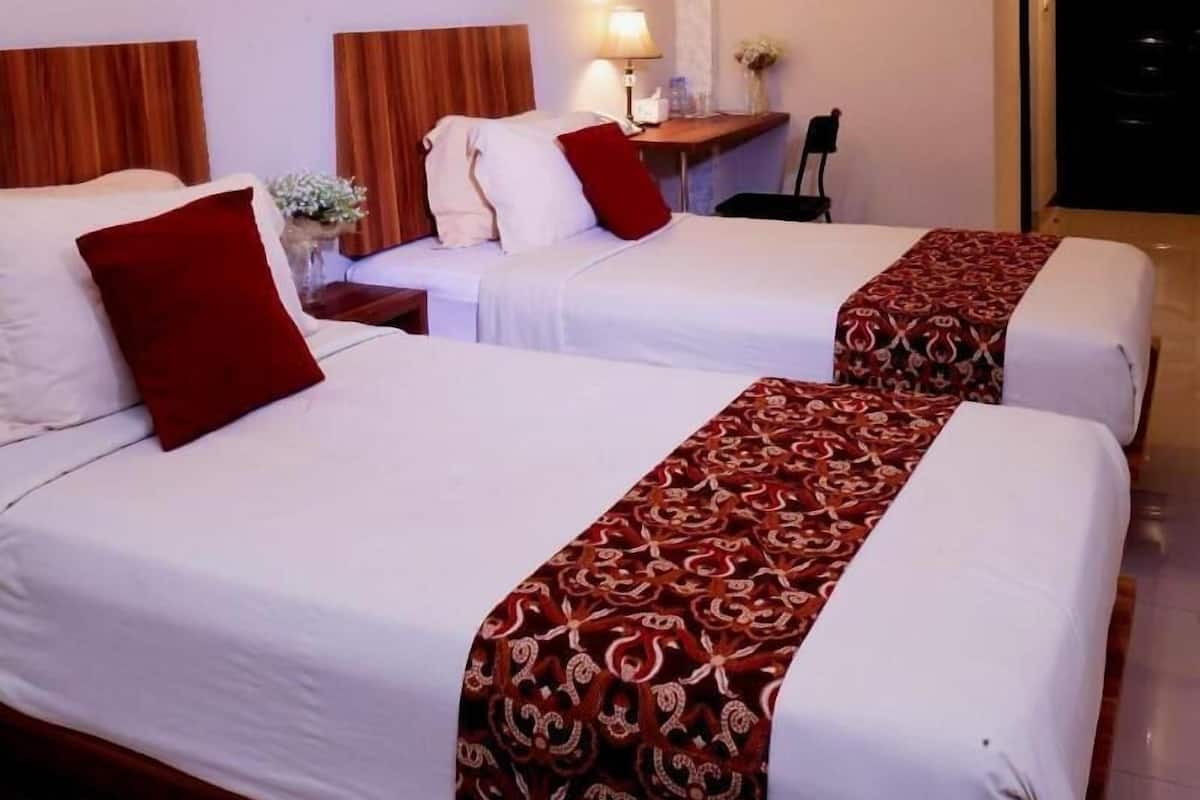 A hotel room with two beds, a desk with a lamp, and an air conditioning unit.