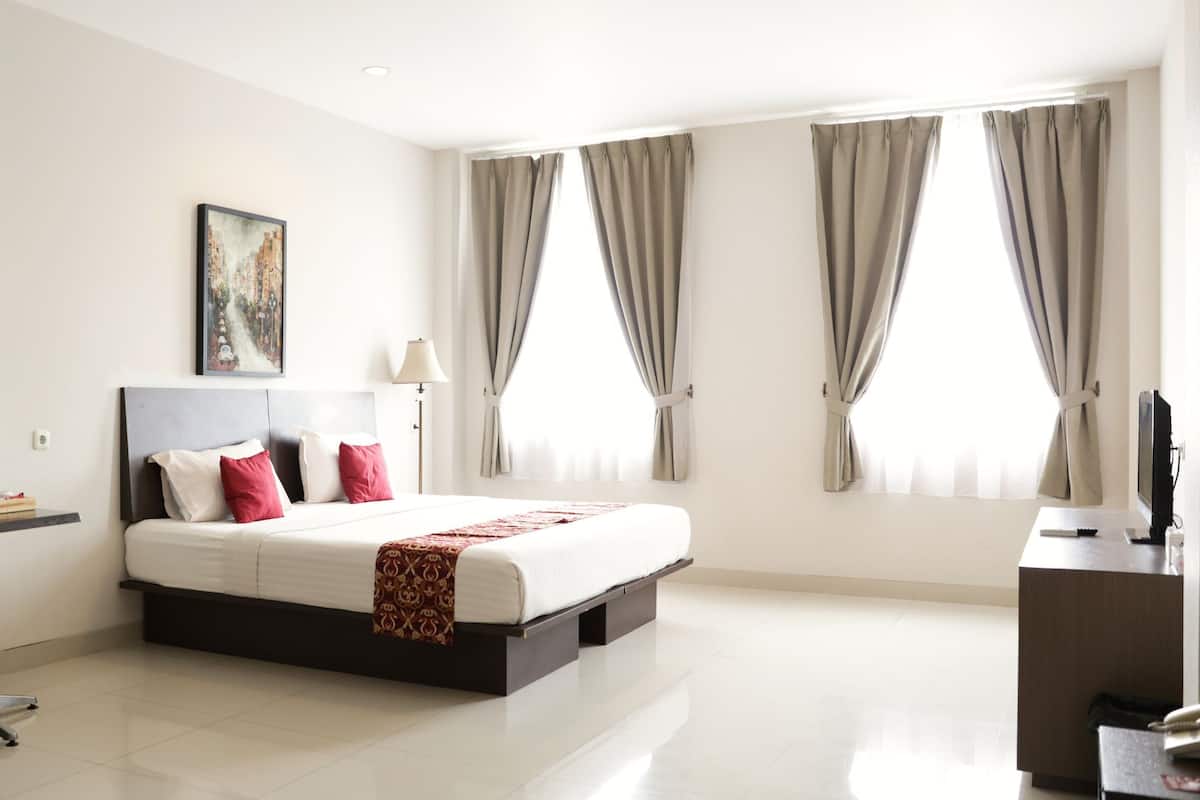 A modern hotel room with a large bed, a desk, a chair, and a television.