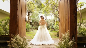 A bride in a white gown standing at the entrance of a wooden archway, surrounded by greenery. - Bale Ocasa (Tangerang)