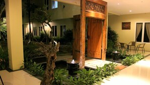A well-lit indoor garden with a water feature, wooden door, and seating area. - Bale Ocasa (Tangerang)