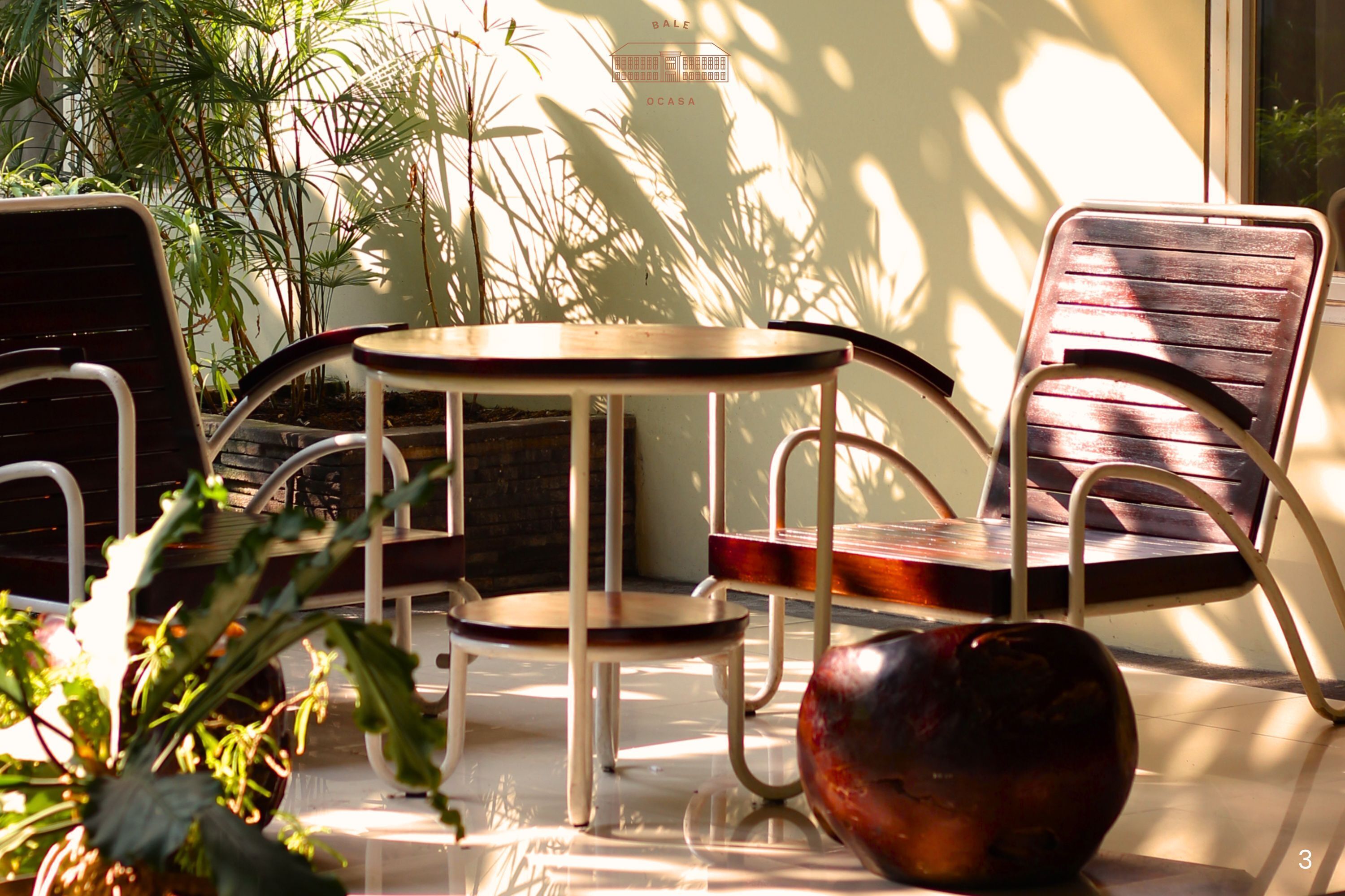 A sunlit patio with a round table and two chairs, surrounded by potted plants.
