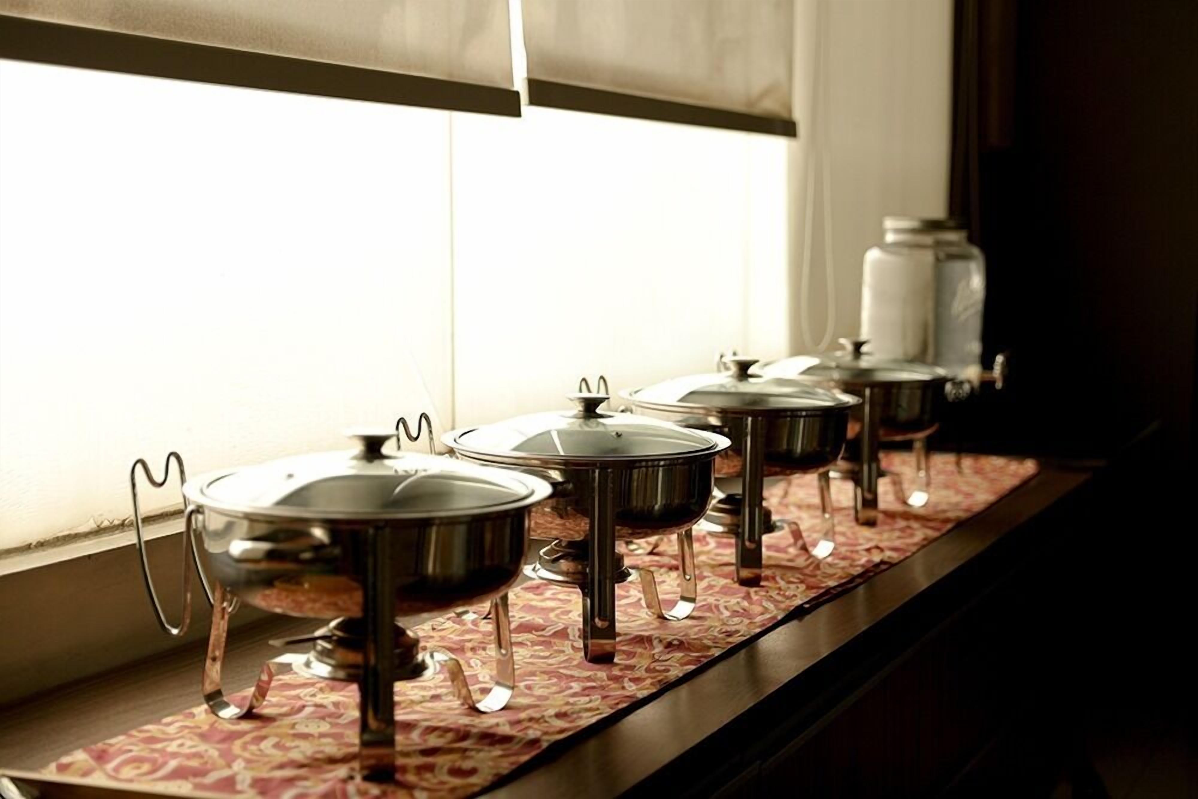 A row of stainless steel pots on a window sill with a patterned tablecloth.