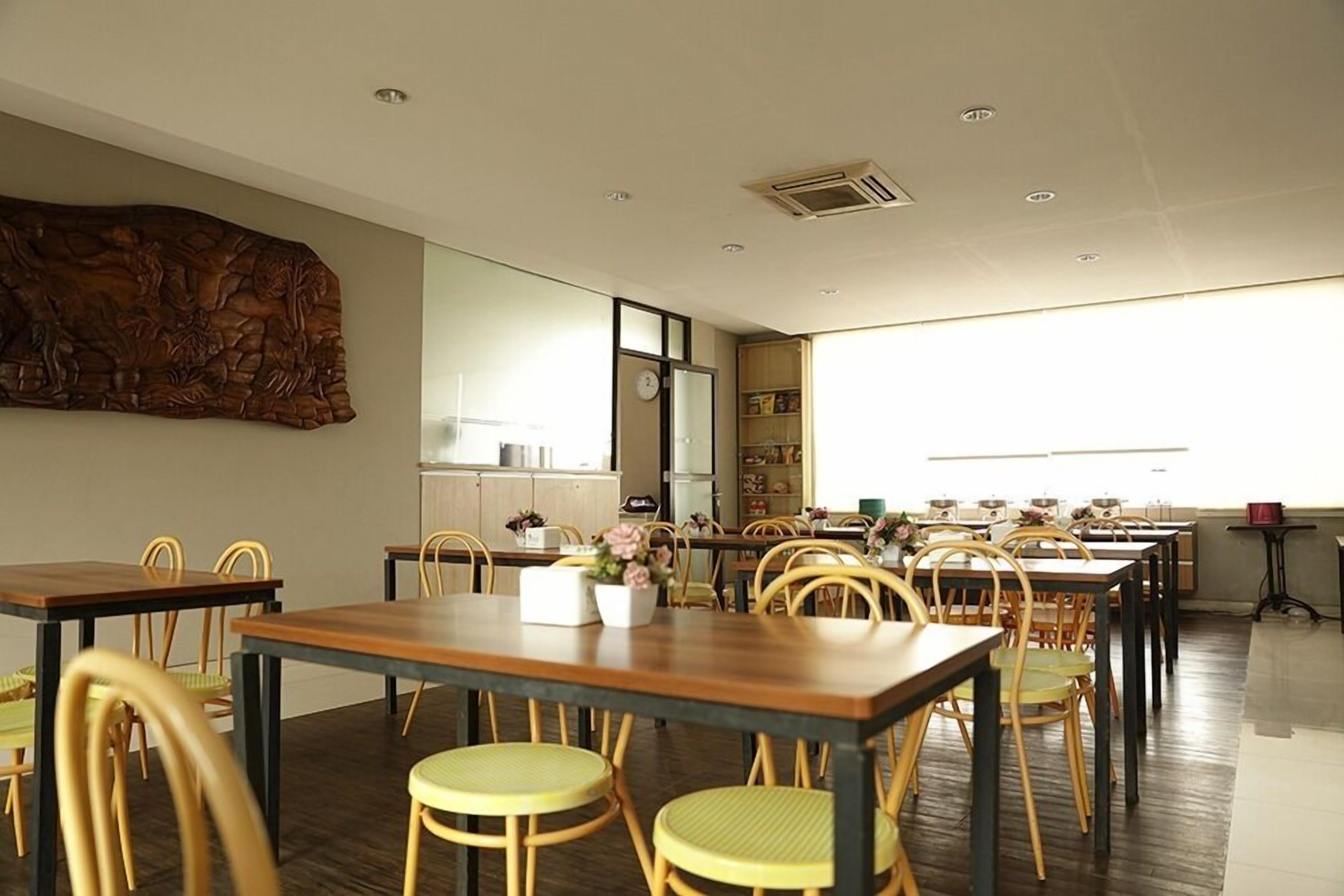 A spacious dining area with multiple wooden tables and chairs, a large decorative wall piece, and a view of the kitchen area.
