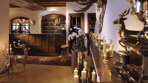 A bar area with wooden paneling, a chandelier, and a display of antlers and deer figurines. - Hotel Arlberg (Lech am Arlberg)
