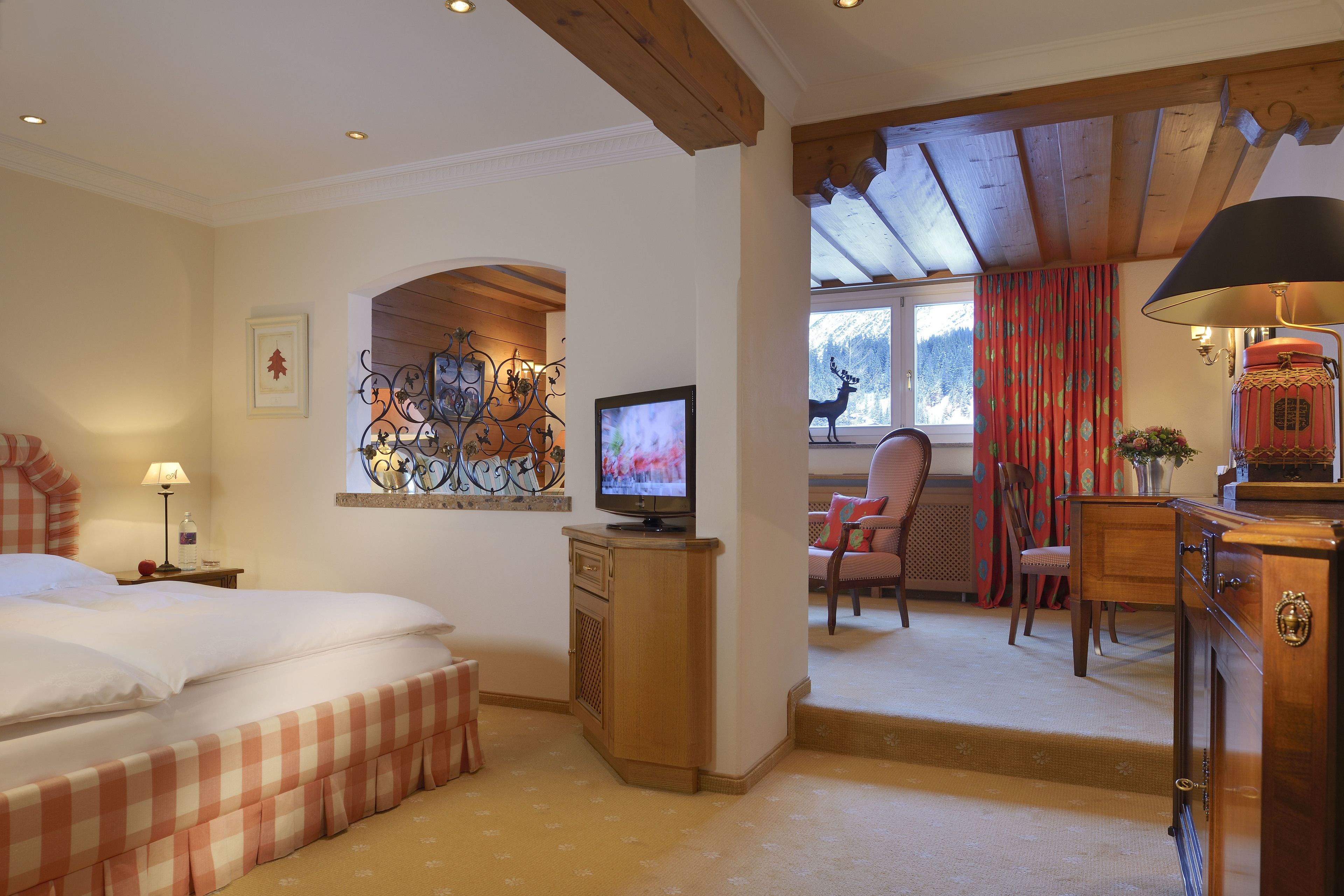 A hotel room with a bed, a television, a desk with a lamp, and a view of the outdoors.