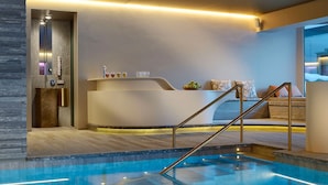 A modern indoor pool area with a reception desk, a staircase, and a seating area with cushions. - Hotel Arlberg (Lech am Arlberg)