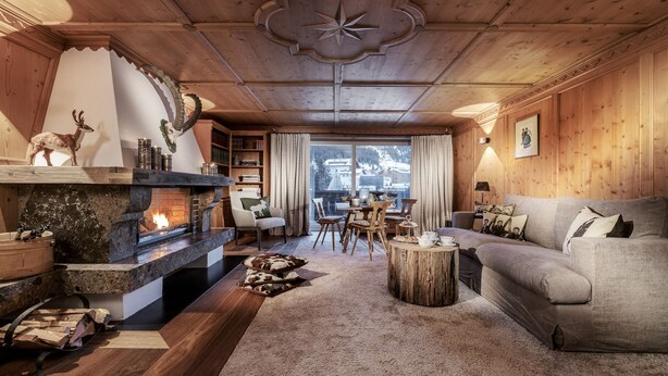 A cozy living room with a fireplace, wooden ceiling, and a view of a snowy landscape. - Hotel Arlberg (Lech am Arlberg)