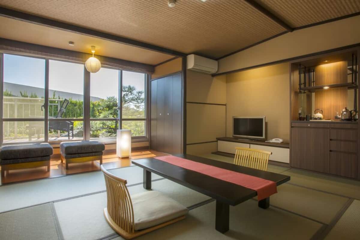A traditional Japanese room with tatami flooring, a low table, cushions, a television, and a kitchen area.
