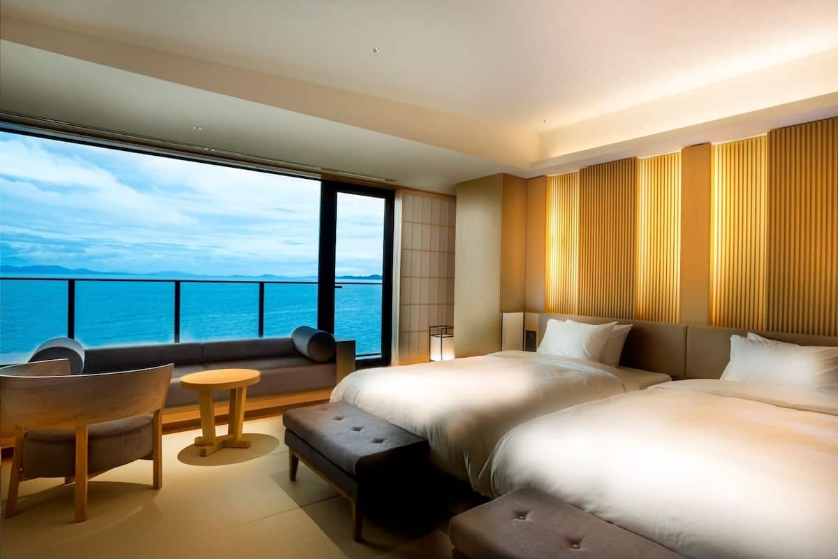 A hotel room with a large bed, a sofa, a small table, and a view of the sea.