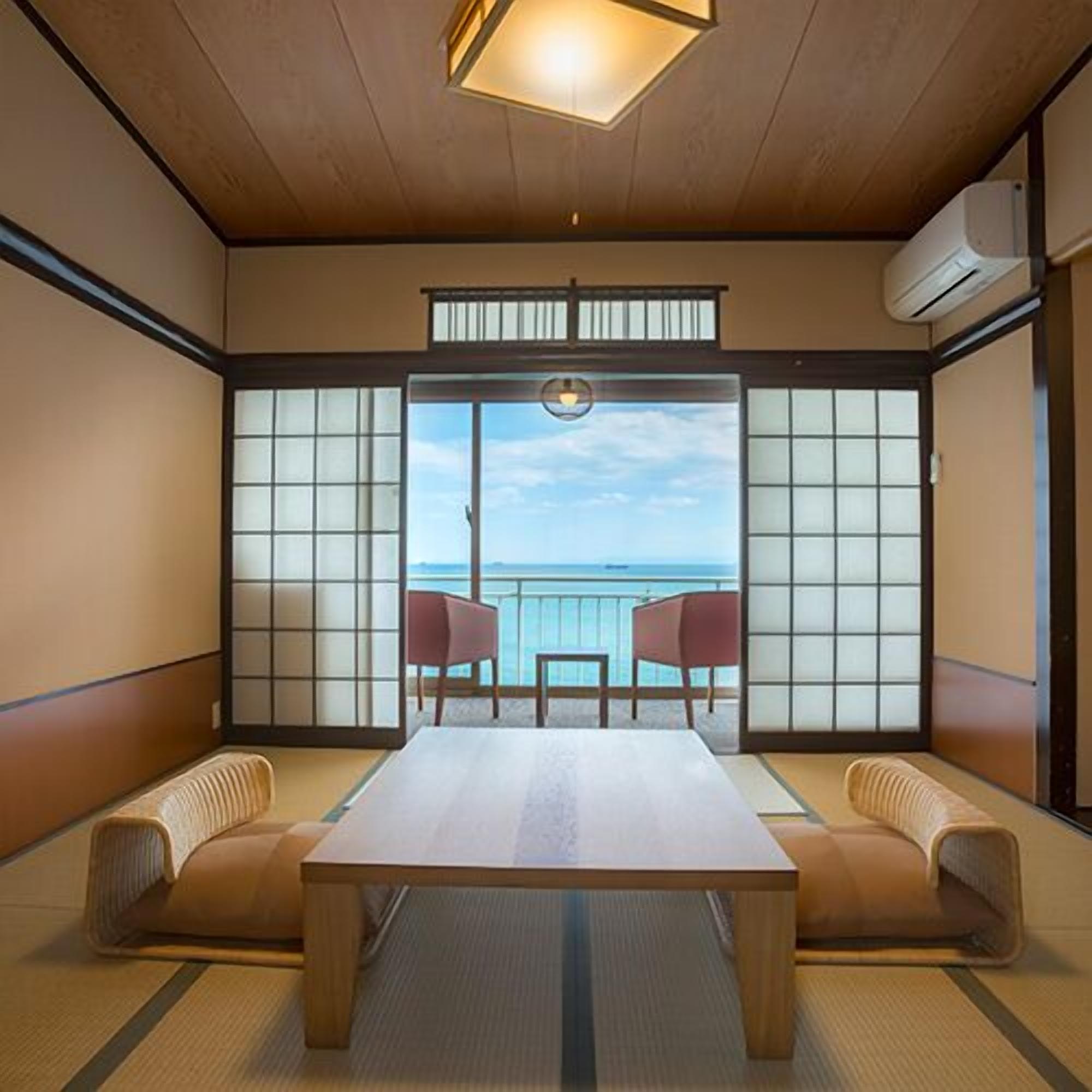 Una habitación japonesa tradicional con suelo de tatami, una mesa baja y puertas correderas que dan a un balcón con vistas al mar.