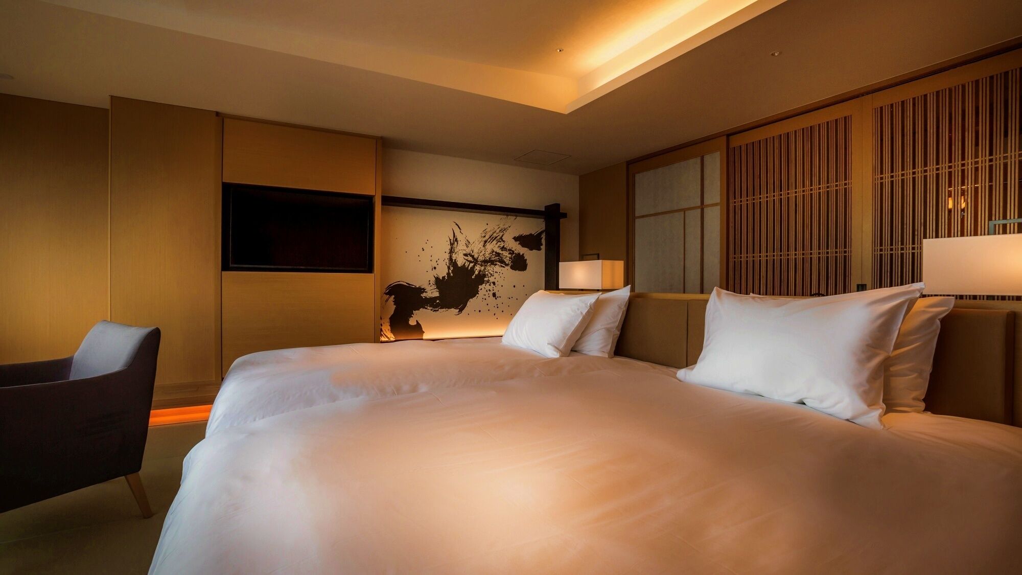 Habitación de hotel con una cama grande, un escritorio, una silla, un televisor y una pared con un panel decorativo.