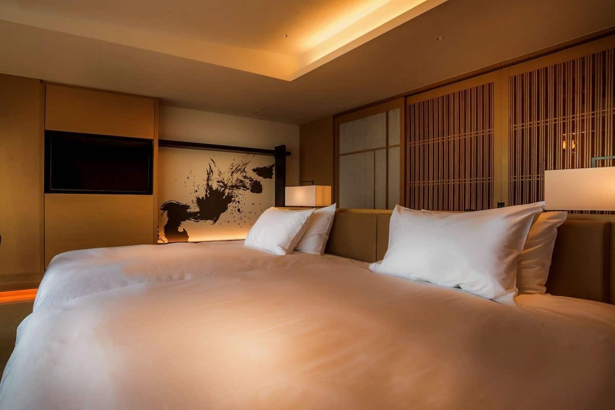 A hotel room with a large bed, a desk, a chair, a TV, and a wall with a decorative panel.