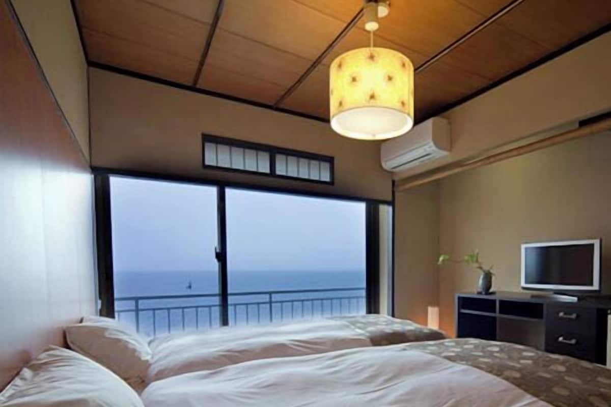 A bedroom with a large bed, a television, and a view of the sea.