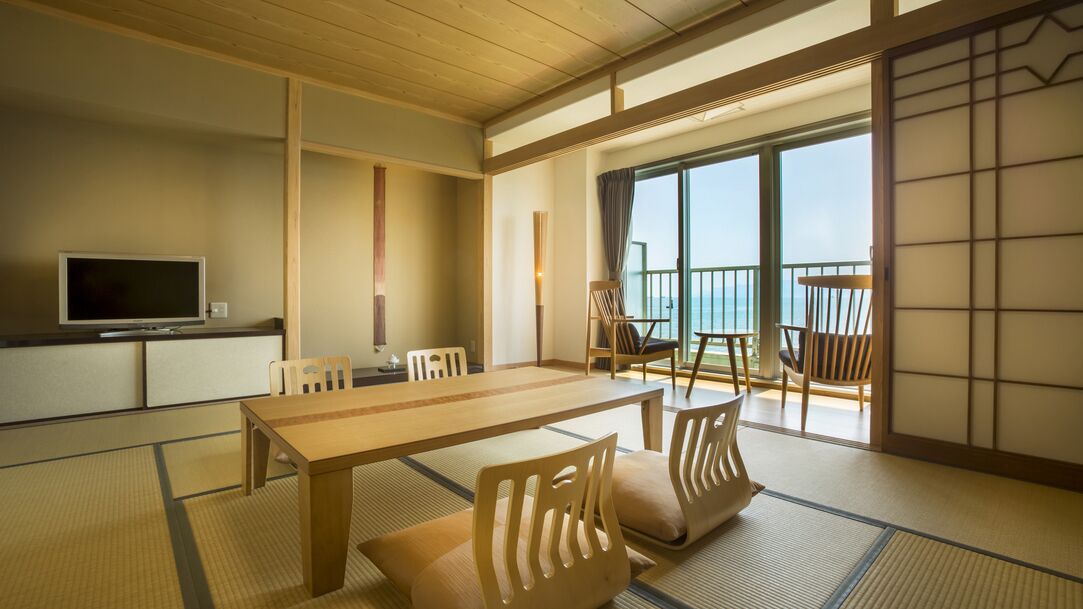 A traditional Japanese room with tatami flooring, a low table, chairs, a TV, and a sliding door leading to a balcony.