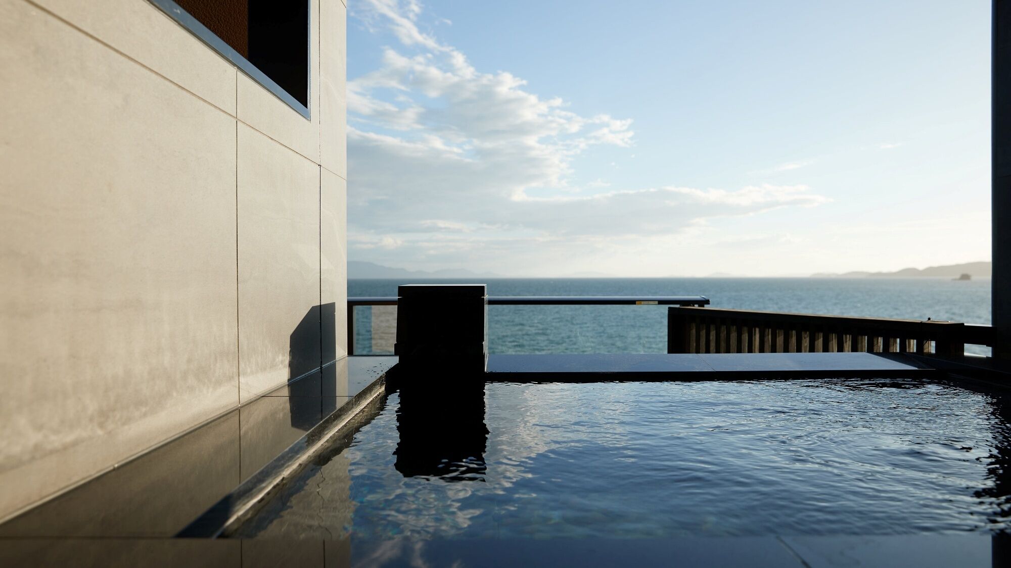 Un edificio moderno con piscina que se extiende hasta la orilla, una terraza de madera y vistas al mar.