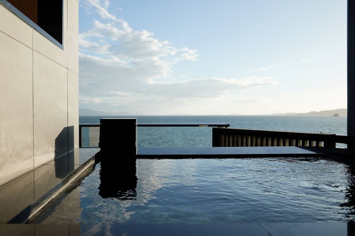A modern building with a pool extending to the water's edge, a wooden deck, and a view of the sea.