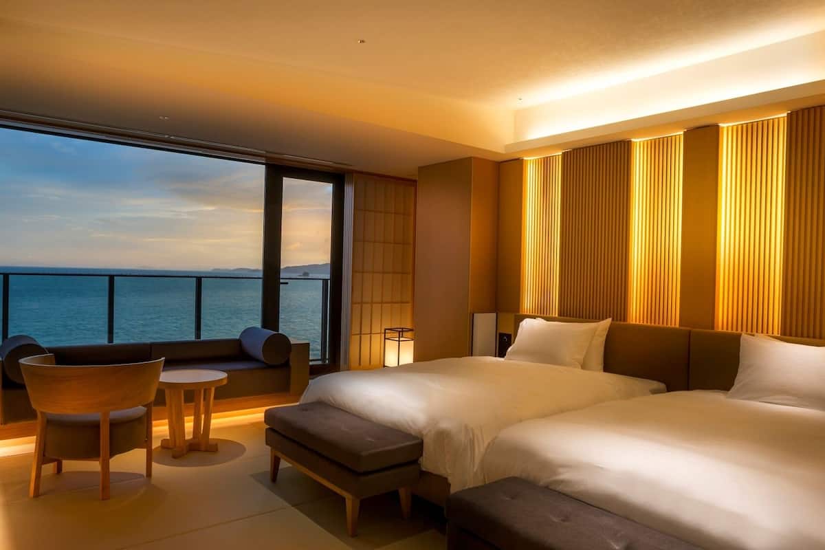 A hotel room with a large bed, a seating area with a table, and a view of the sea.