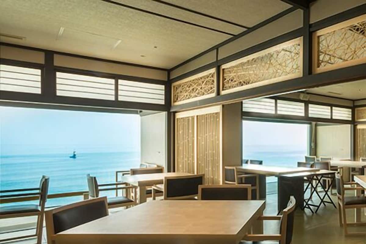 A room with a large window overlooking the sea, wooden furniture, and a view of the ocean.