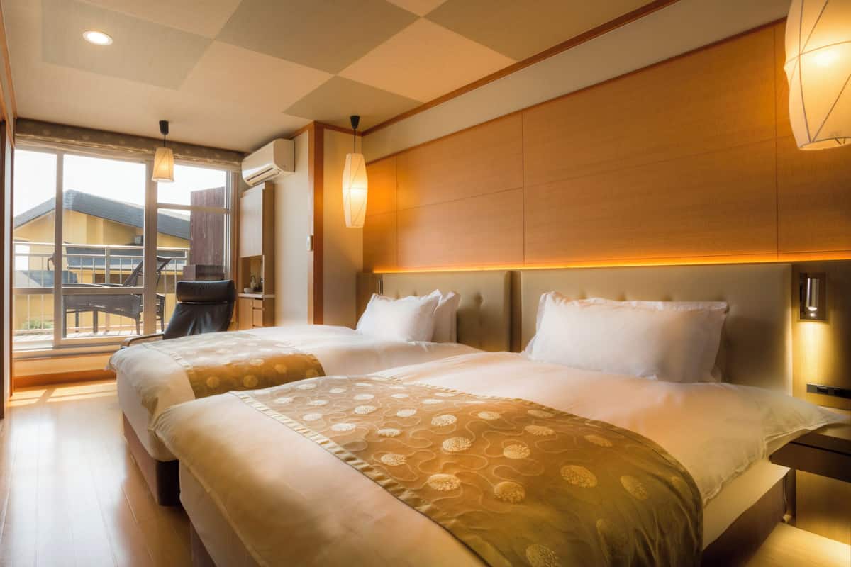 A hotel room with two beds, a balcony, and a view of a building.