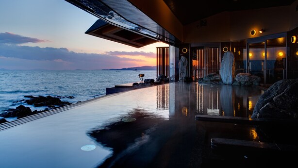 Una piscina infinita moderna con vista al océano al atardecer.