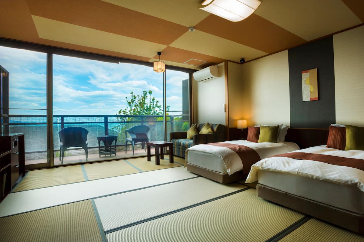 A hotel room with two beds, a balcony with a view, and a traditional Japanese tatami mat floor.