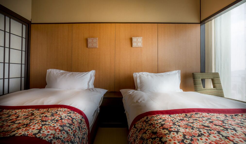 A hotel room with two beds, wooden headboard, floral bedspreads, and a window with sheer curtains.