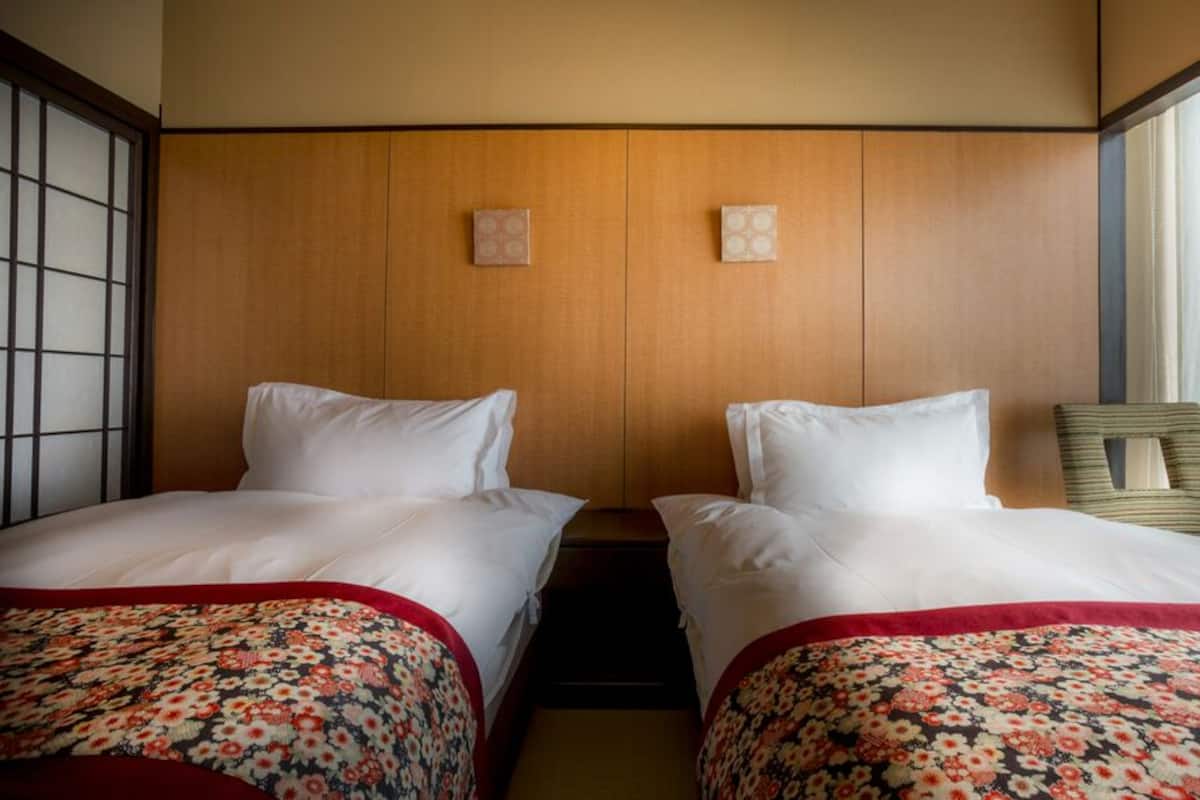 A hotel room with two beds, wooden headboard, floral bedspreads, and a window with sheer curtains.