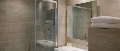 A modern bathroom with a glass-enclosed shower, a large mirror, and a white sink.