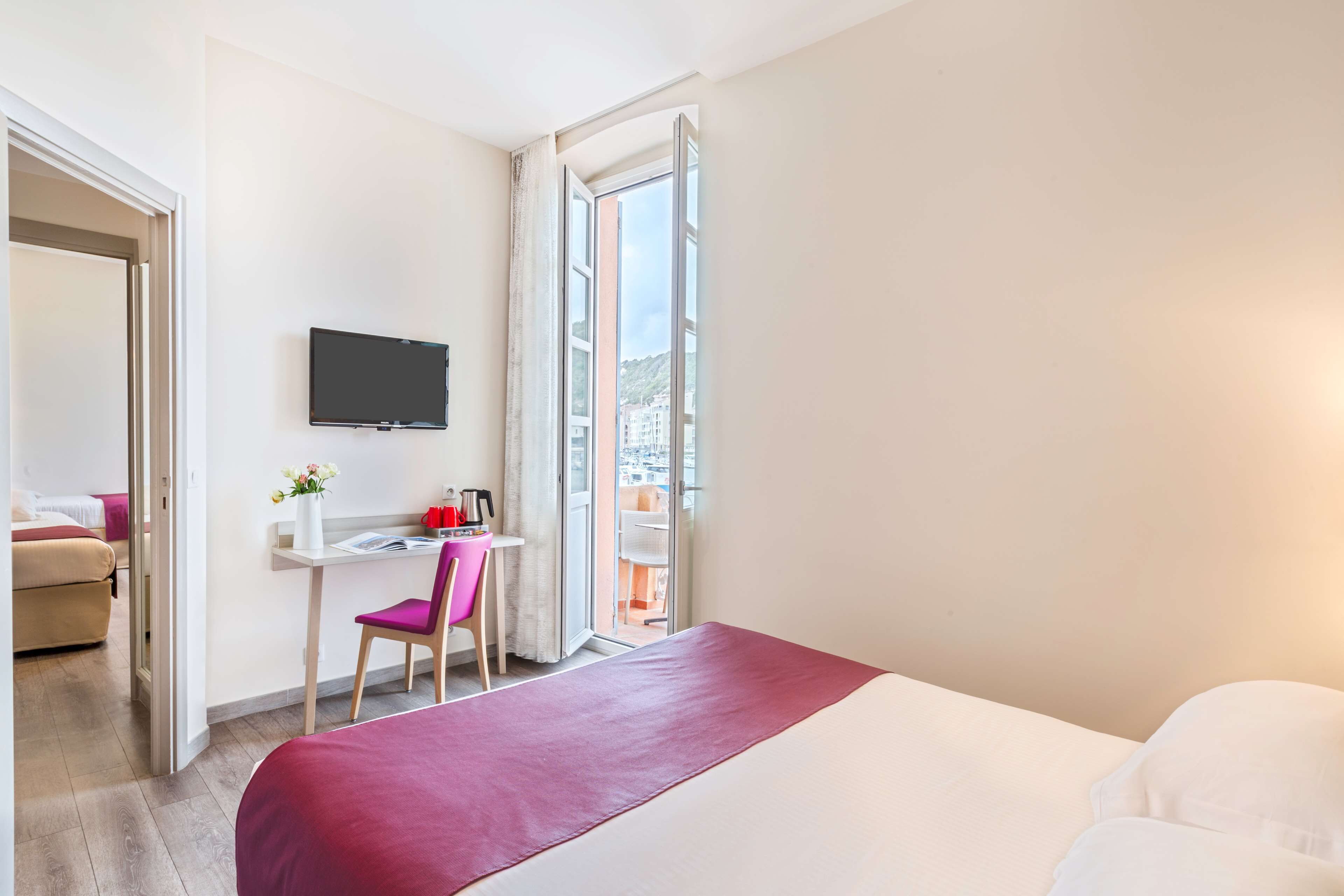 Habitación de hotel con cama, escritorio con silla, televisor y ventana con vistas a edificios.