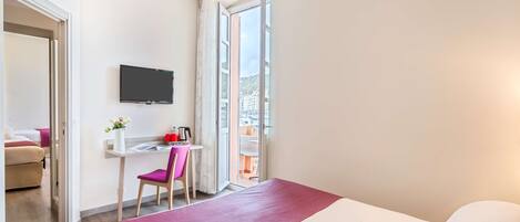 Habitación de hotel con cama, escritorio con silla, televisor y ventana con vistas a edificios.