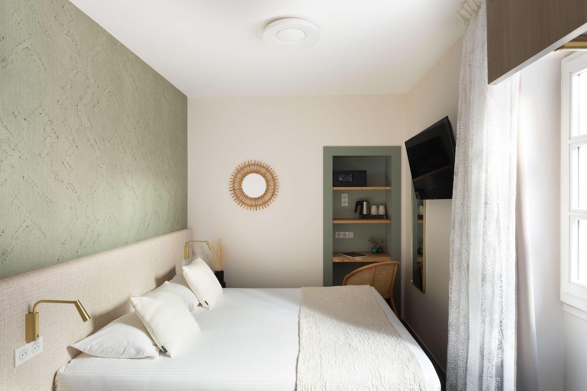 Een netjes opgemaakt slaapkamer met een bed, bedlampen, een wandtelevisie en een klein wandrek met spullen.