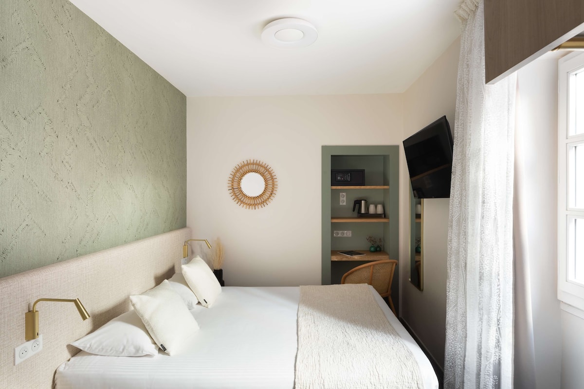 Une chambre à coucher bien rangée, avec un lit, des lampes de chevet, un téléviseur fixé au mur et une petite étagère sur laquelle sont posés quelques objets.