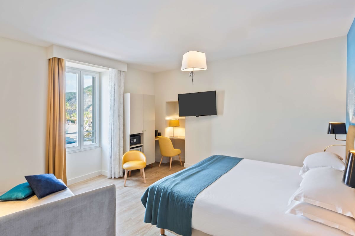 Une chambre d’hôtel avec un lit, un bureau et une chaise, une télévision et une fenêtre avec des rideaux.
