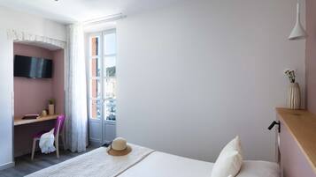 A bedroom with a bed, a desk with a chair, a TV mounted on the wall, and a window with curtains.