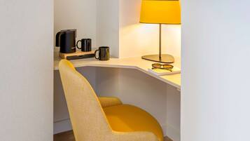 A corner desk with a yellow chair, a coffee maker, two mugs, a lamp, and a pair of glasses.