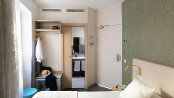 Une chambre d’hôtel avec un lit, une armoire, un miroir et une salle de bain visible à travers une porte ouverte.