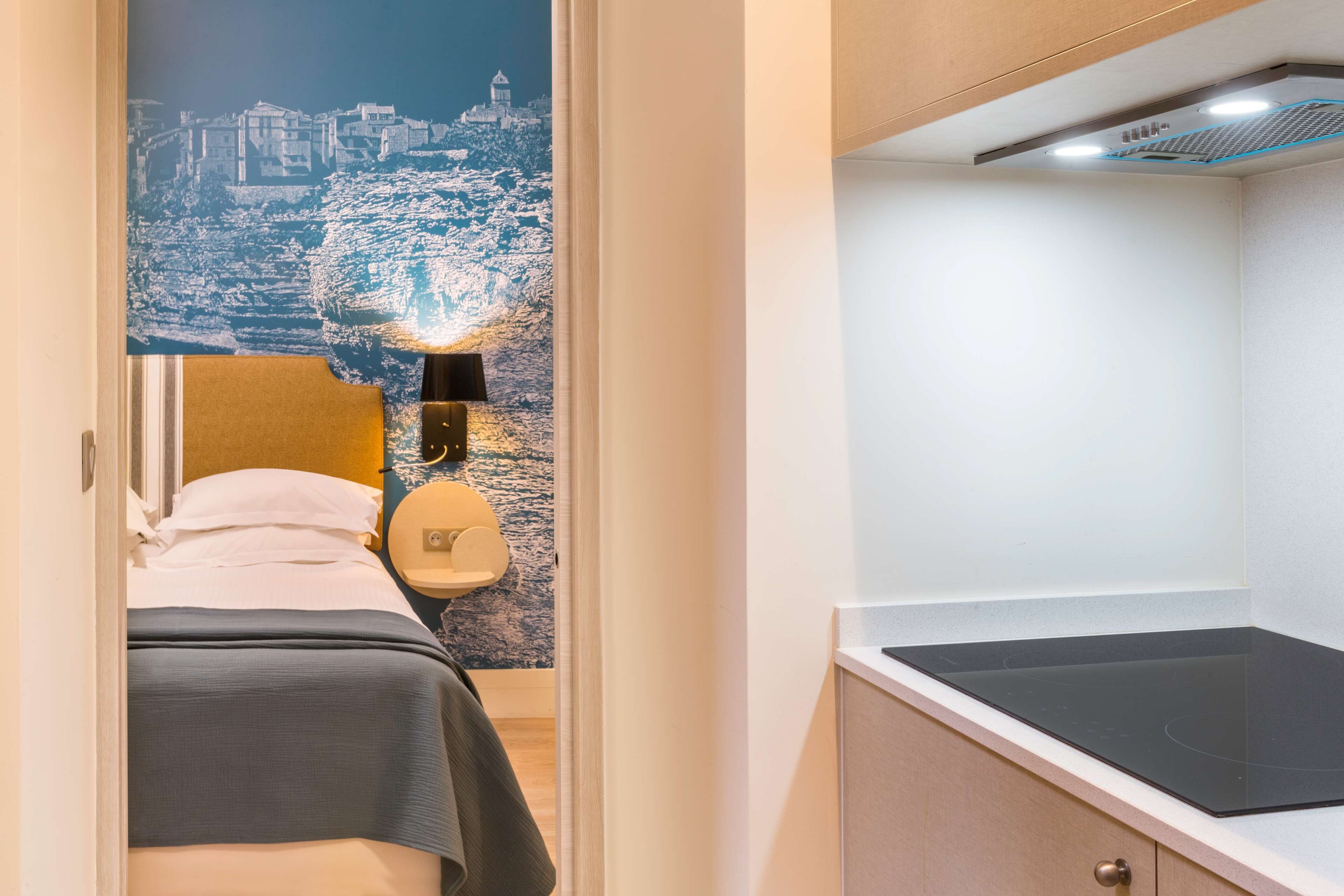 A bedroom with a bed, a nightstand, a wall-mounted lamp, and a cityscape mural.