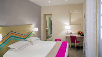 Habitación de hotel con cama, escritorio, silla, espejo y ventana con cortinas.