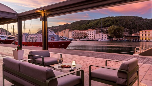 A waterfront terrace with outdoor seating, a view of boats, and buildings in the background. - Best Western Hotel Du Roy D'aragon (Bonifacio)