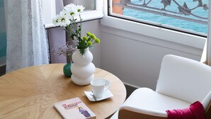A room with a view of boats at a marina, a white chair, a wooden table with a vase of flowers, and a book. - Best Western Hotel Du Roy D'aragon (Bonifacio)