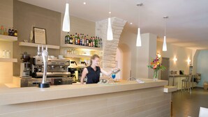 A modern bar area with a bartender preparing a drink, a coffee machine, and a variety of bottles on shelves. - Best Western Hotel Du Roy D'aragon (Bonifacio)