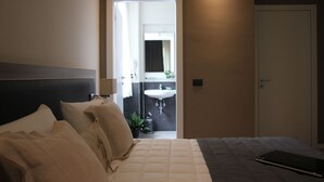 A hotel room with a bed, a bedside table, a lamp, a potted plant, and a bathroom visible through an open door. - Hotel Zara Milano (Milan)