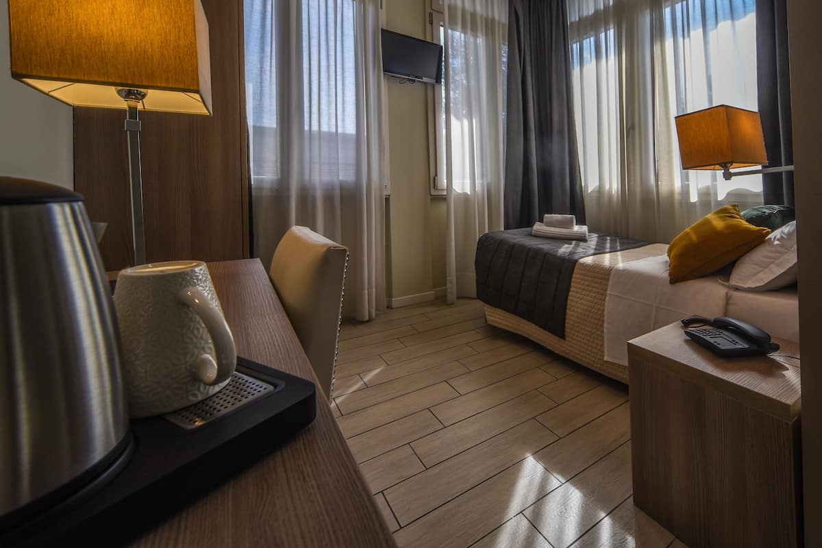 A hotel room with a bed, a desk with a lamp, a chair, a television, and a coffee maker.