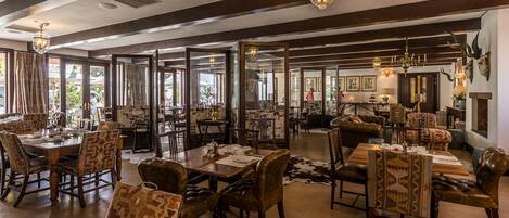 A spacious dining area with high ceilings, large windows, and a mix of wooden and upholstered furniture.