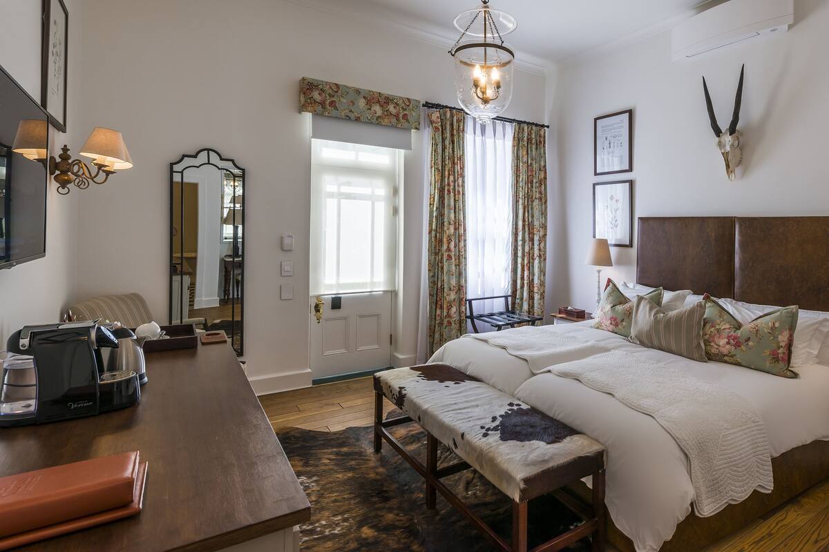 A bedroom with a bed, bedside table, lamp, and a desk with a coffee maker.