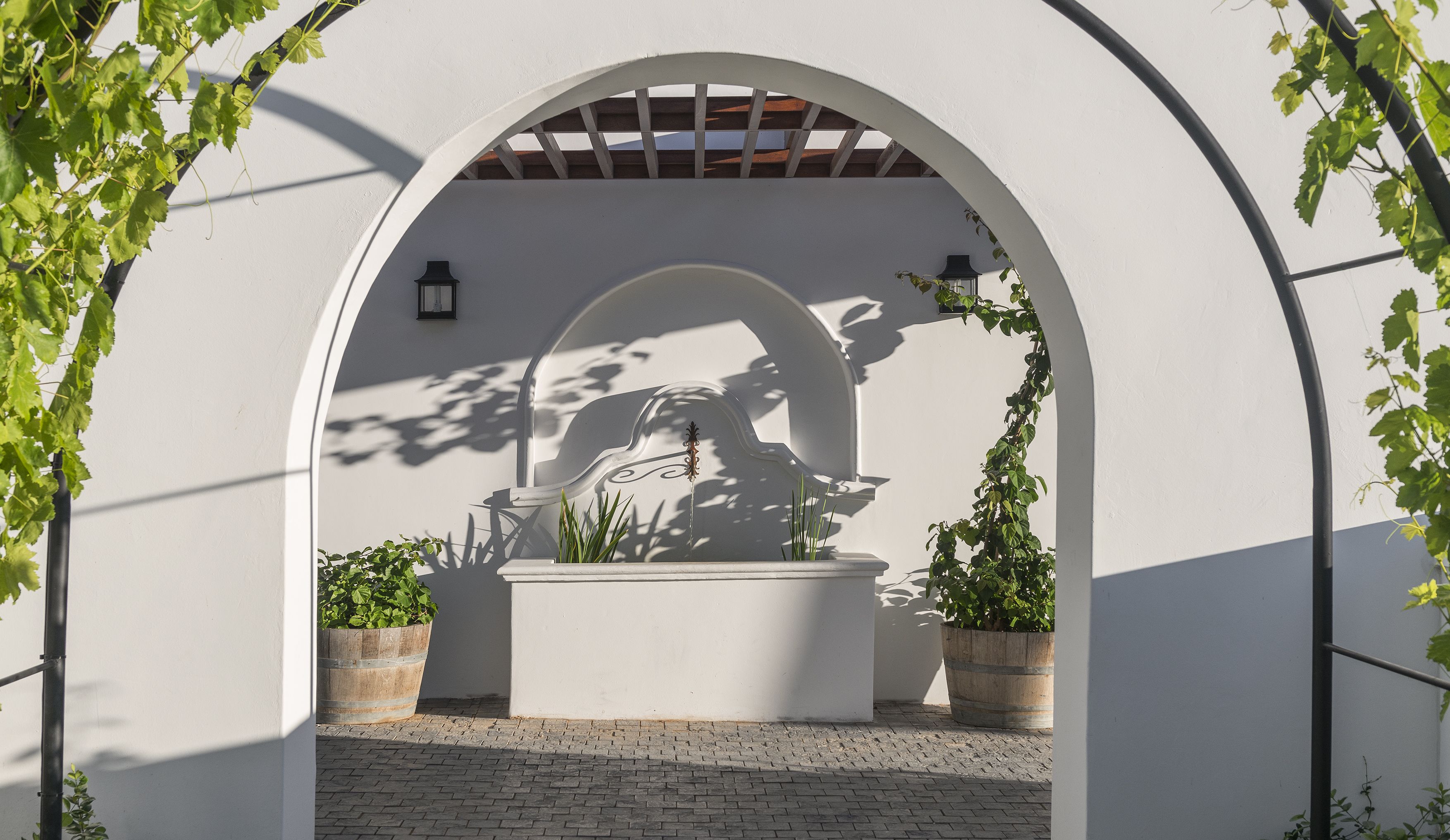 An arched architectural feature with a decorative element, potted plants, and a lantern.