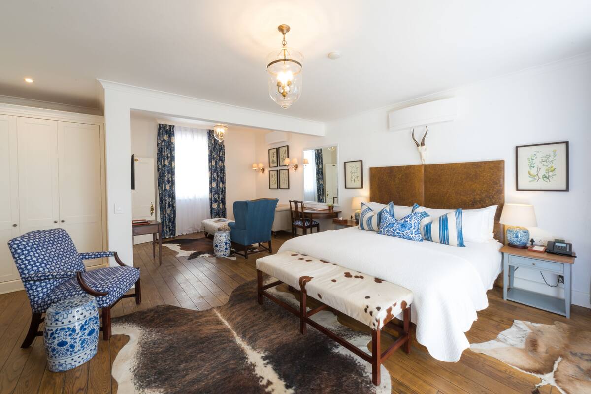 A bedroom with a large bed, a wooden bench, a chair, a desk, and a lamp.