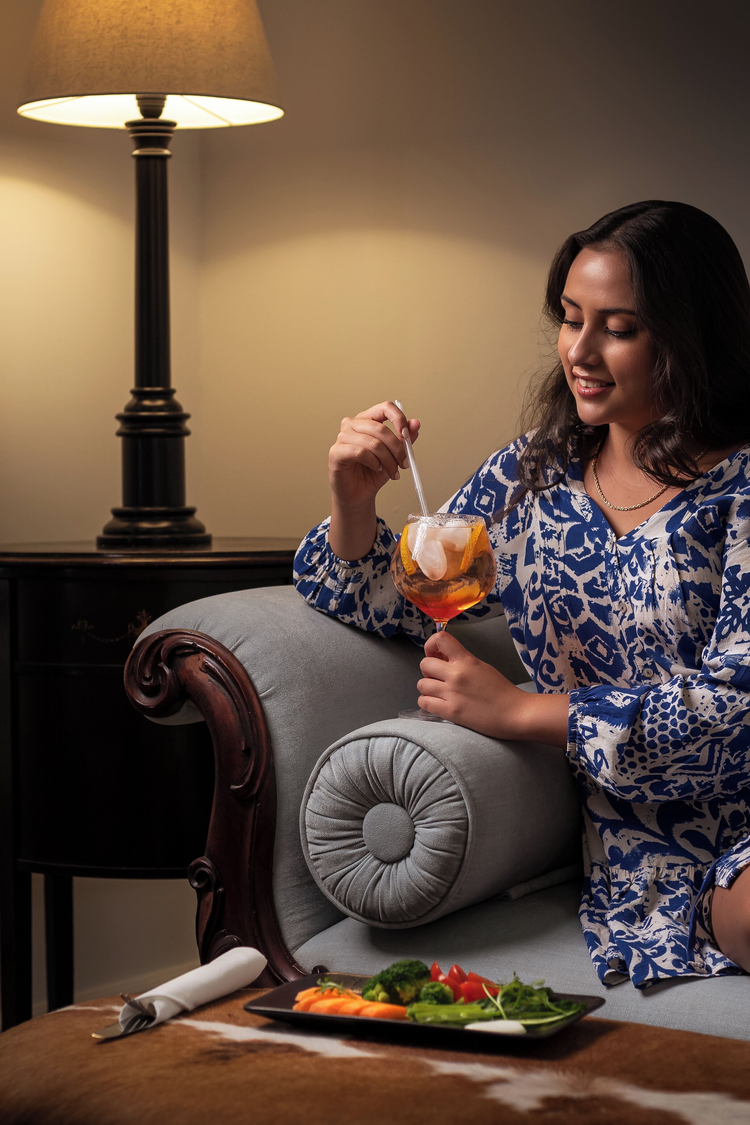 A person sitting on a grey upholstered chair with a plate of vegetables in front of them.
