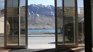 A view through a glass door with a mountain and lake in the background. - Hildibrand Hotel (Fjardabyggd)